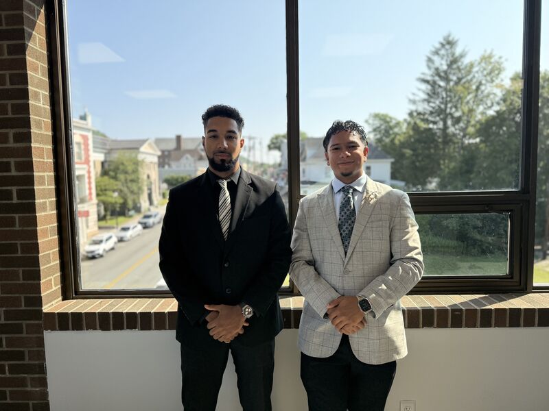 Two well-dressed team members standing confidently by a sunlit office window
