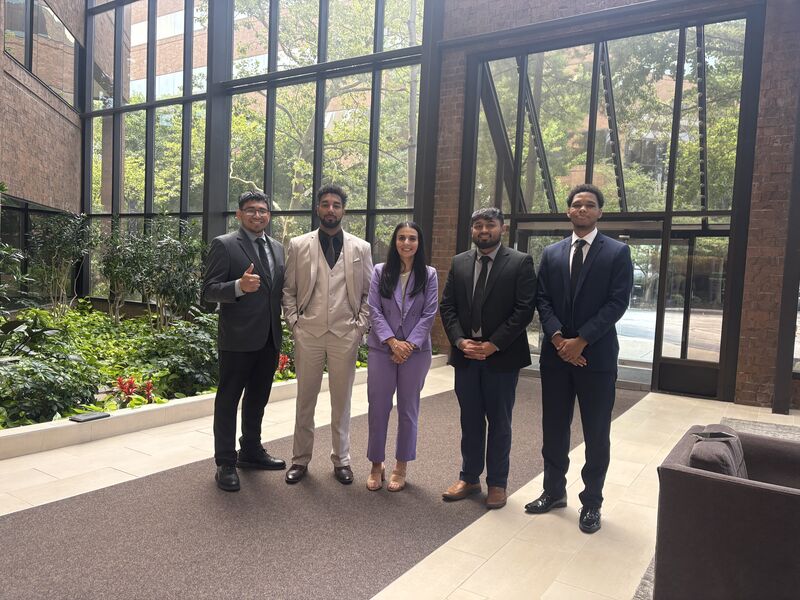 Five professionally dressed team members standing together in a glass atrium