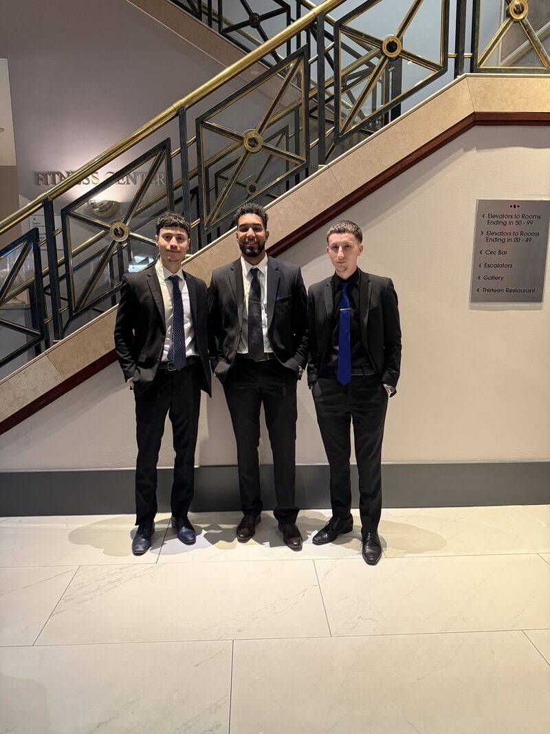 Three confident team members in business attire by a staircase